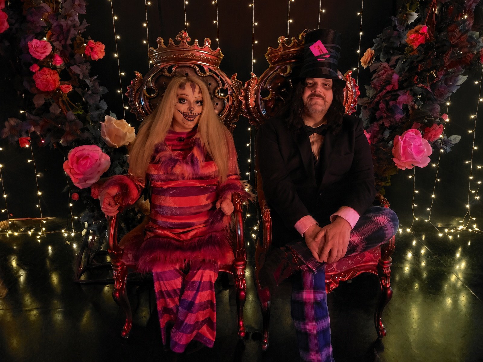 A Cheshire Cat and a Mad Hatter seated on ornate gilded thrones amid roses and fairy lights at Underland