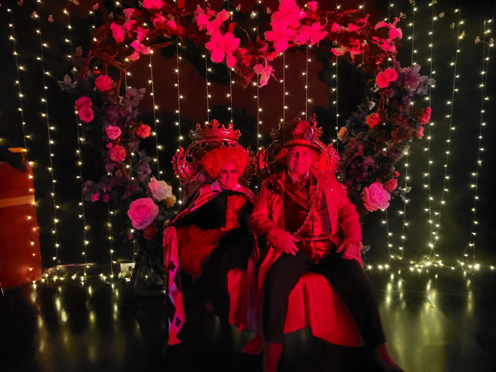 The Queen of Hearts and King of Hearts in red costume beneath the rose and fairy light heart arch at Underland