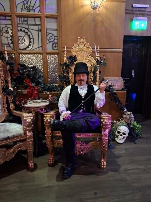 A guest in top hat and purple velvet holding court on an ornate gilded throne at the Vampire Ball